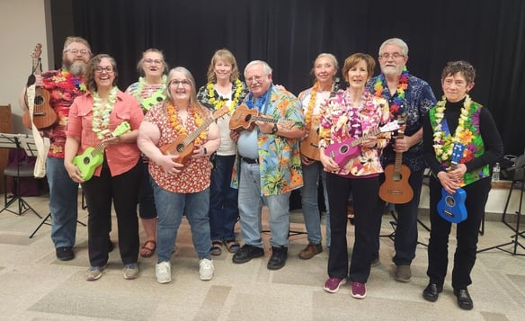 A group of older adults pose with their Ukuleles during a Hawaiian-themed performance.