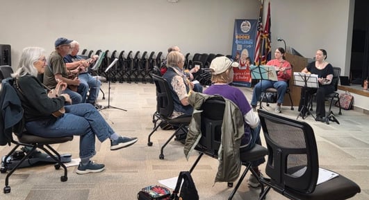 A group of older adults practice ukulele while listening to two instructors.